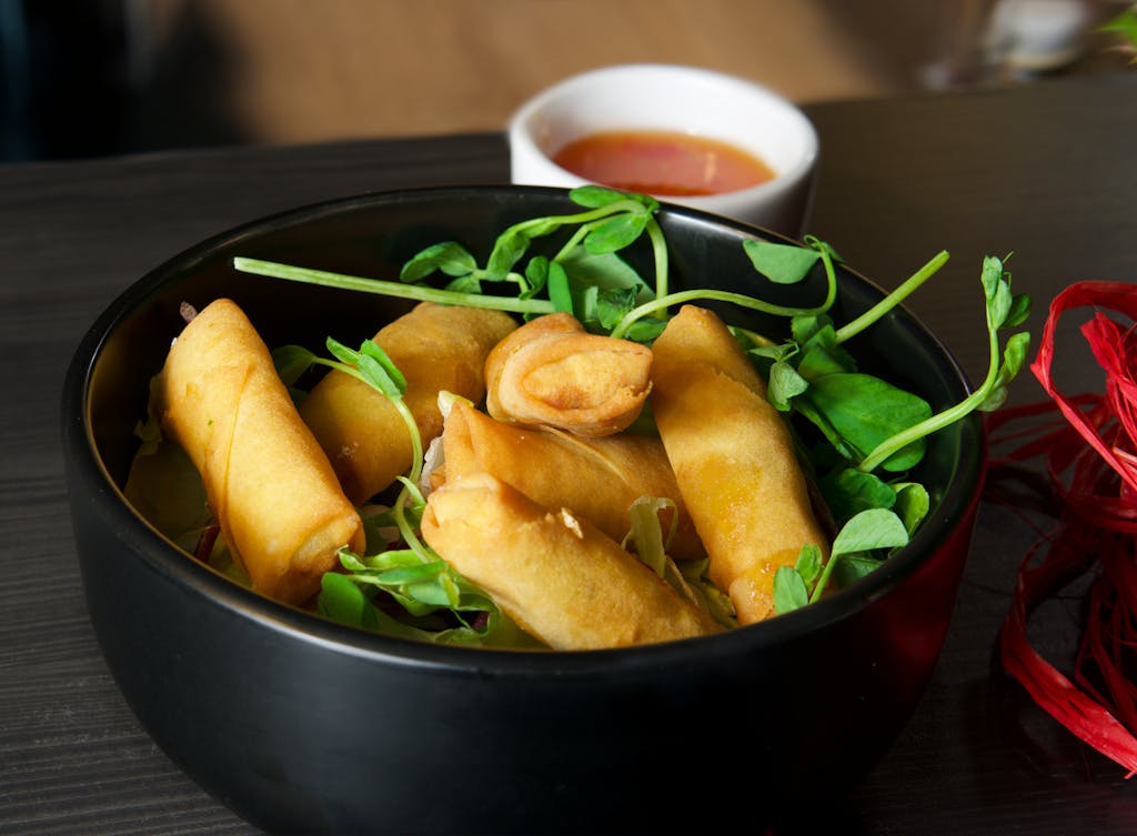 Crispy vegetarian spring rolls served with a dipping sauce, garnished with fresh greens.